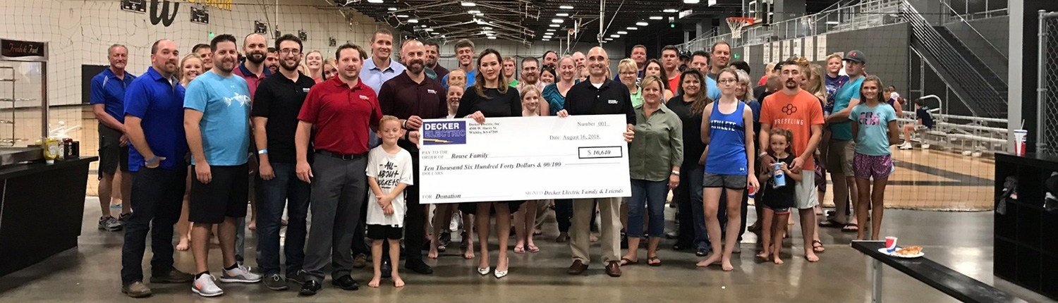 Large crowd of Decker Electric staff with check presentation to local family at trampoline park